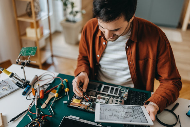 年轻人拿着数码平板电脑在家修理笔记本电脑图片下载