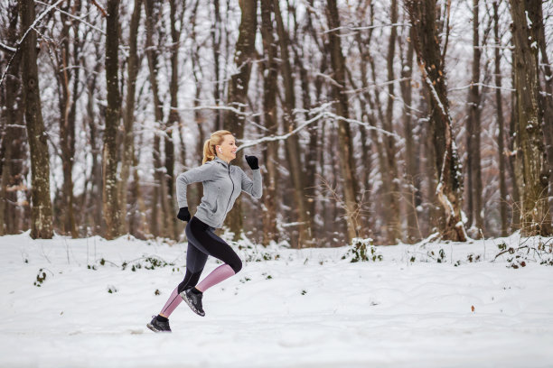 快速的女运动员在温暖的运动服在森林中奔跑在冬天的自然雪地里。有氧运动，冬季健身，寒冷天气图片下载