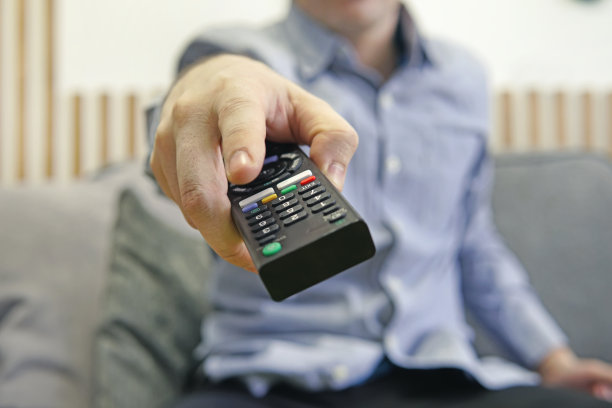 手里拿着遥控器的人在看体育频道时按下了遥控器上的按钮。遥控器在手中特写。切换频道。图片下载