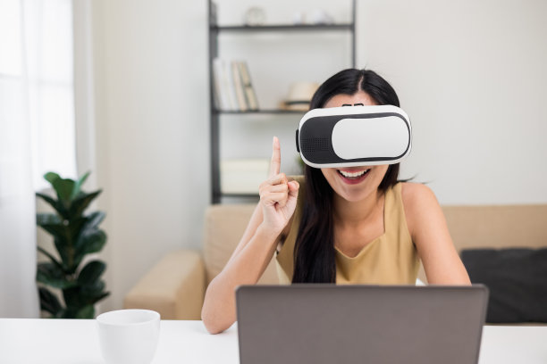 年轻的亚洲女性戴上虚拟现实眼镜，坐在家里的客厅里参加虚拟模拟世界在线聊天会议。职场女性在社交媒体上的会议。图片下载
