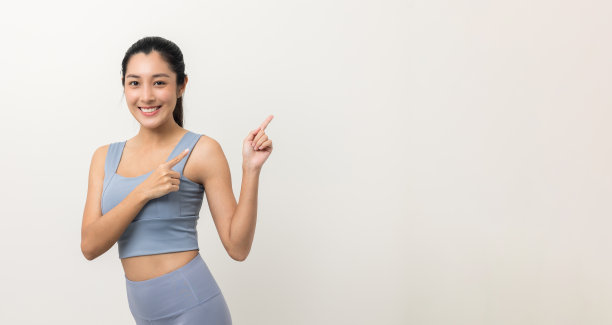 年轻美丽的亚洲妇女与运动服装在孤立的白色背景。人像运动妇女站姿势锻炼锻炼在工作室。手指指向空白的广告文字。图片下载