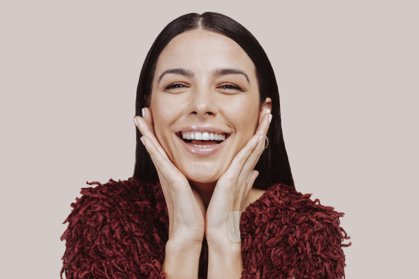 年轻美丽快乐的女人看着镜头在工作室与手在脸颊图片下载