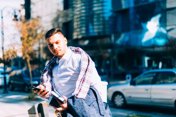 一个年轻的商人正走在市中心，手里拿着笔记本和咖啡，环顾四周图片下载