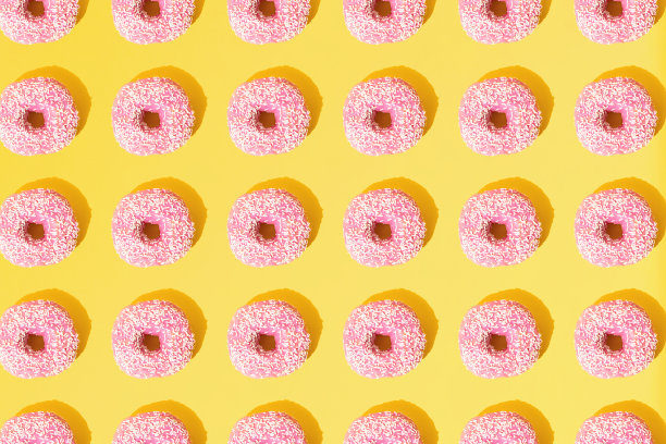 粉红色的环形甜甜圈。黄色粉彩背景上的小白色碎屑。模式。平的。图片下载