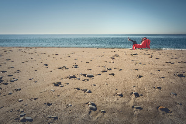 女孩在冬天的阳光下晒太阳，躺在沙滩上的沙滩椅上，用红色的毛巾图片下载