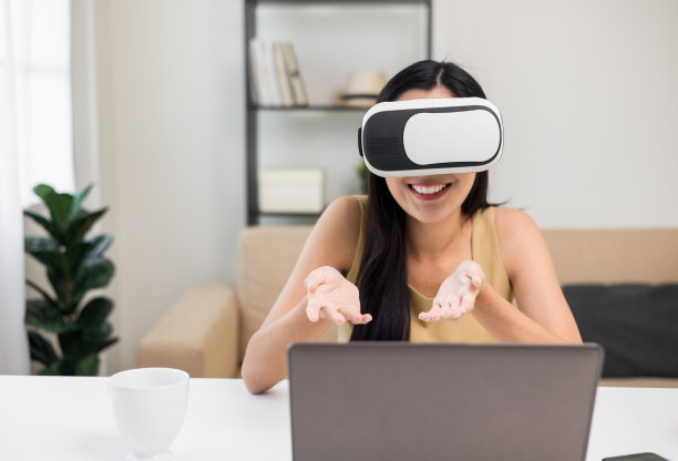 年轻的亚洲女性戴上虚拟现实眼镜，坐在家里的客厅里参加虚拟模拟世界在线聊天会议。职场女性在社交媒体上的会议。图片下载