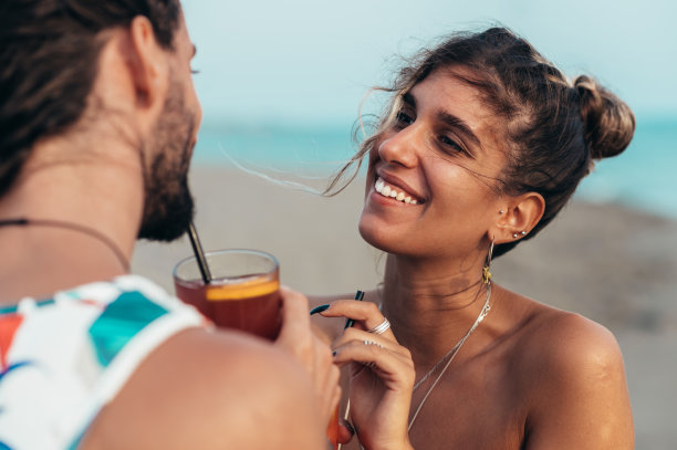 迷人的年轻夫妇带着酒精鸡尾酒在海滩上散步图片下载