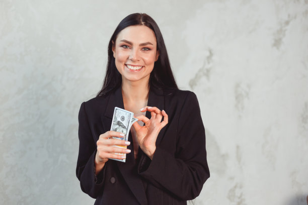 年轻漂亮的黑发女人，穿着正式的黑色西装，手里拿着美元钱。激情与诱惑观念图片下载