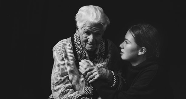一位年长的妇女和一个成年孙女坐在一起，背景是黑色的。黑白照片。图片下载