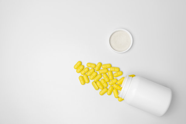 一个装着黄色药丸的白色罐子，从容器里掉了出来。俯视图，复制空间。图片下载