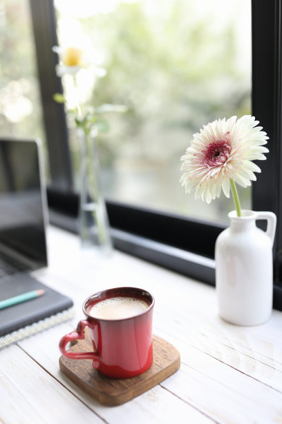红色的咖啡杯和一瓶非洲菊在木桌上图片下载
