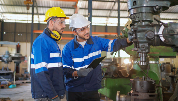 工程师在生产线上走动，讨论工厂的机器或设备。佩戴安全帽和眼镜，防止事故发生。工业、维护和技术理念。图片下载