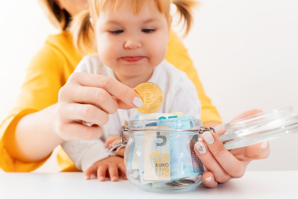 女婴和她的母亲把比特币和货币放在一个玻璃罐里。关闭了。投资和网上银行的概念图片下载