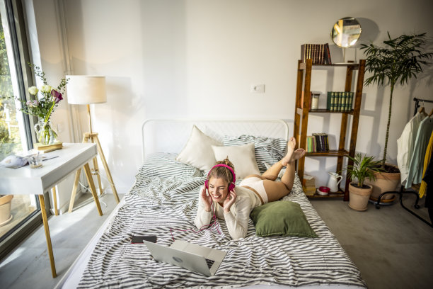 美丽微笑的女人戴着耳机躺在床上图片下载