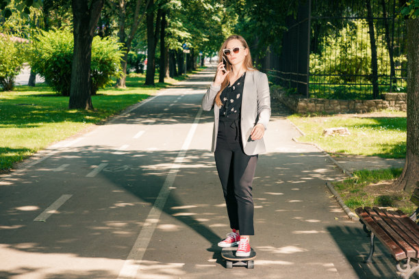 年轻的商业女孩的肖像驾驶滑板通过公园图片下载