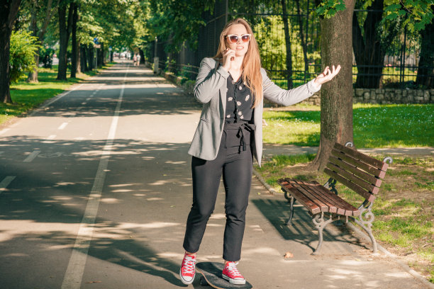 甜美的女孩在公园里一边打手机一边玩滑板图片下载