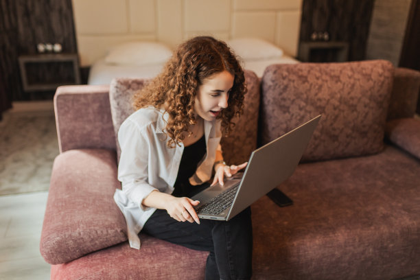 电子商务。学生在笔记本电脑上工作。红发卷发女孩在家里的电脑上工作。疯子喜欢好的工作。商业项目的胜利。快乐的情绪。庆祝胜利。商业成就图片下载