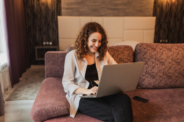 电子商务。学生在笔记本电脑上工作。红发卷发女孩在家里的电脑上工作。疯子喜欢好的工作。商业项目的胜利。快乐的情绪。庆祝胜利。商业成就图片下载