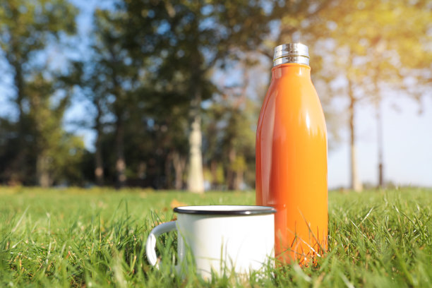现代的橙色热水瓶和杯子在户外绿色的草地上。空间的文本图片下载