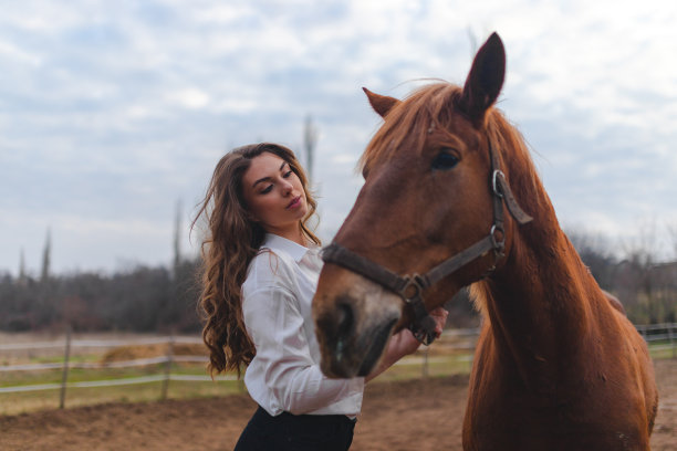 一个年轻的白人妇女，穿着白衬衫，抱着她的棕色的马在农场里图片下载