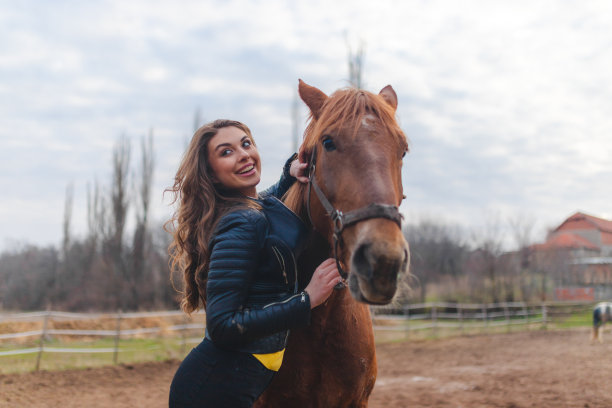 在农场上，一名年轻的白人妇女穿着皮夹克，拥抱着她的棕色马图片下载