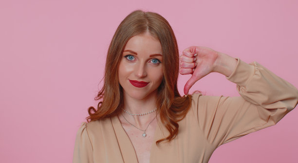 沮丧的女孩穿米色上衣，拇指向下的手势，不赞成，不满意，不喜欢图片下载