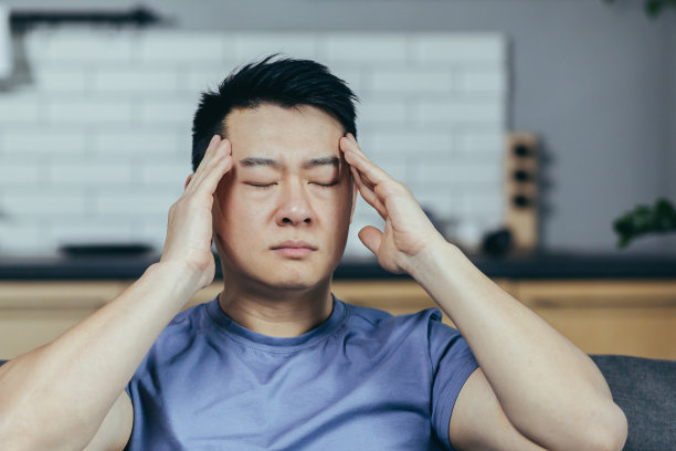 亚洲人一个人在家，累了，生病了，他头痛，坐在沙发上，把他的手放在脑后。一个精疲力竭的病人的特写照片图片下载