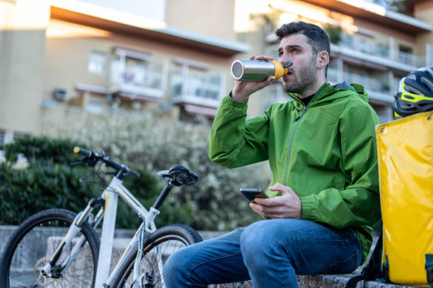 年轻的快递员在休息，快速快递服务人员从自己的烧瓶中饮水，交通行业的可持续发展和生态工作，金属塑料免费食堂图片下载