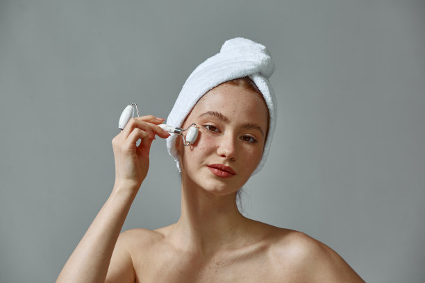 漂亮的年轻女孩在毛巾按摩脸颊玉滚轮按摩健康的肤色。面部按摩、拉皮图片下载