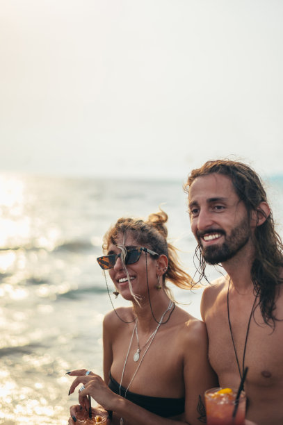 迷人的年轻夫妇带着酒精鸡尾酒在海滩上散步图片下载