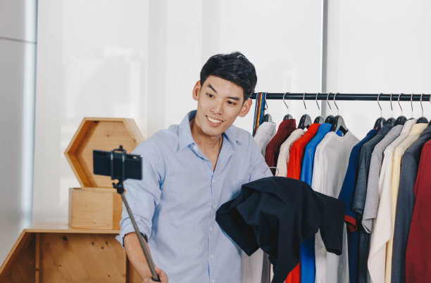 一名年轻的亚洲男子博主正在播放一段网上卖衣服的视频。图片下载