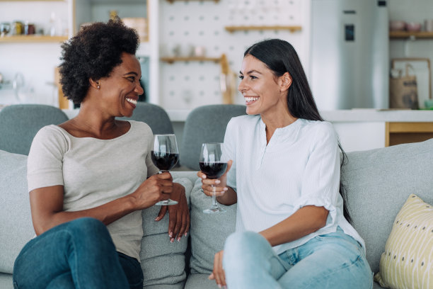 两个年轻的女人在家里放松的时候喝酒。图片下载