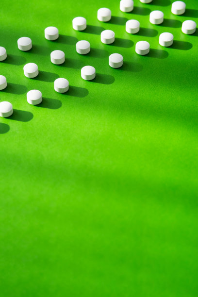 白色药丸或维生素胶囊图案在绿色背景，复制空间。膳食补充剂支持健康。图片下载