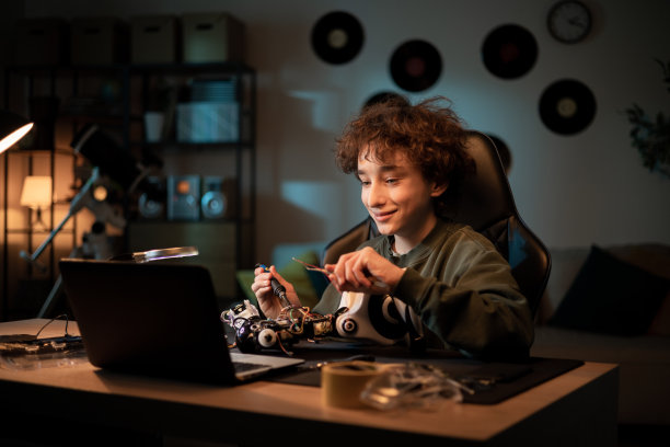 男孩通过笔记本电脑上的网络摄像头和朋友聊天，展示他是如何学习焊接电子产品的，吹嘘机器人项目，解释玩具遥控的线缆连接图片下载