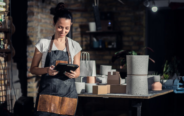 穿着围裙的手工艺人手持牌匾在作坊里的画像。图片下载
