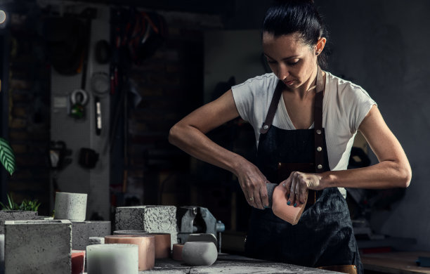 穿着围裙的手工艺人在她的工作室制作装饰混凝土花瓶。图片下载