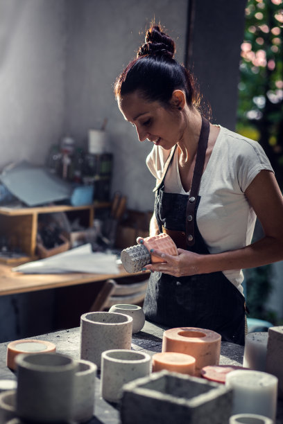 穿着围裙的手工艺人在她的工作室制作装饰混凝土花瓶。图片下载