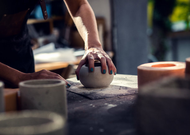 近距离拍摄手工艺人的手在她的工作室制作装饰混凝土花瓶。图片下载
