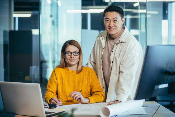 建筑师和设计师的创意团队在一个现代办公室的桌子上工作，亚洲男人和女人微笑着看着相机，纸上的建筑计划图片下载