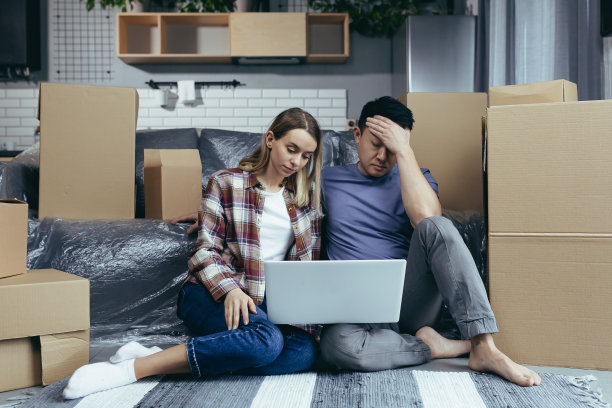 一个年轻的家庭在新公寓里，深思熟虑，认真地在网上商店挑选新家具，坐在地板上的纸箱中间，用一台笔记本电脑图片下载