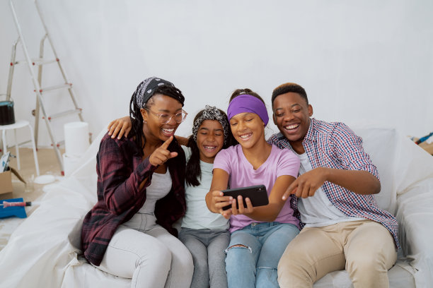 相亲相爱幸福美满的家庭正在装修的公寓里消磨时间，他们在手机上看照片，搞笑的照片，说笑，评论，大笑图片下载