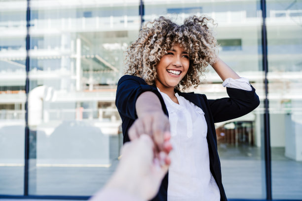 美丽的笑着的商业女人在城市握着朋友。建筑的背景图片下载