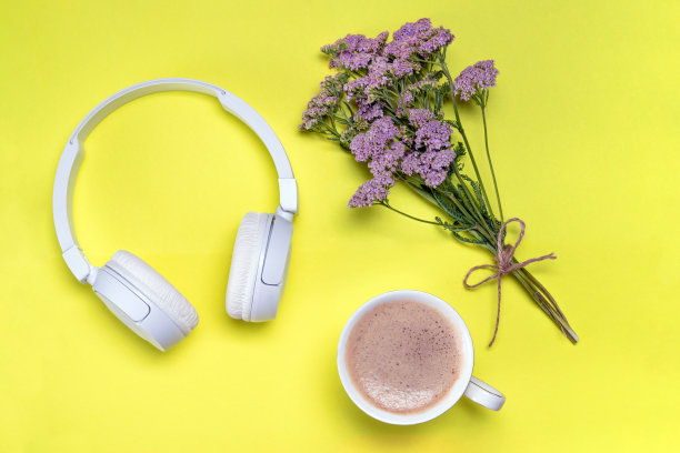早上听音乐放松一下。一杯咖啡，无线耳机，黄色背景上的花朵。图片下载