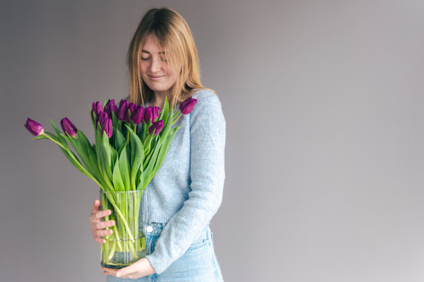 一个年轻女子的肖像与一束郁金香在灰色的背景。图片下载