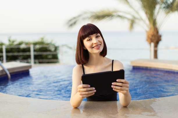 快乐微笑的女孩在游泳池边用数码平板电脑图片下载