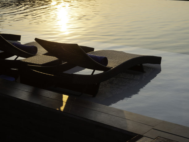 两个空的现代藤日光浴床，床椅客人在白色大理石地板在酒店度假池在宁静的日落天空背景与复制空间，度假的概念。图片下载