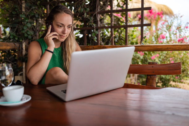 一位女商人坐在木凳上，一边打电话，一边用笔记本电脑。图片下载