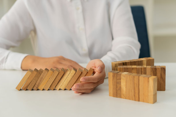 Domino的战斗是颠覆或持续风险和业务策略的结果。女孩的手合在一起，阻止了三个通道之间的木块掉在多米诺骨牌线上。图片下载