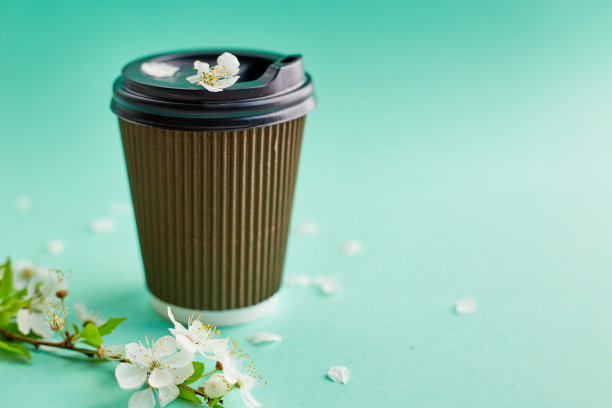 蓝绿色背景上的樱花纸咖啡杯。特写空白牛皮纸咖啡杯图片下载
