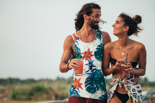 迷人的年轻夫妇带着酒精鸡尾酒在海滩上散步图片下载